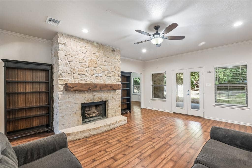 Stone-clad fireplace with a wood mantel, wood-finish flooring, built-in shelving, ceiling fan, and recessed lighting