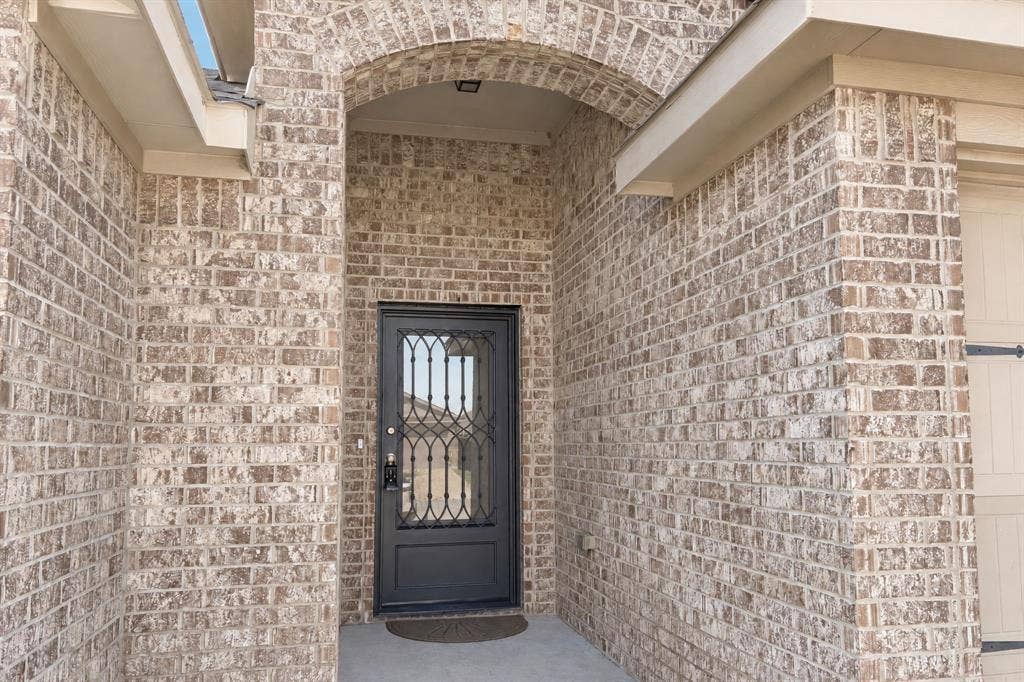 Full-brick exterior featuring an arched entryway, stone-finish masonry, and a black metal-framed glass front door with decorative scrollwork