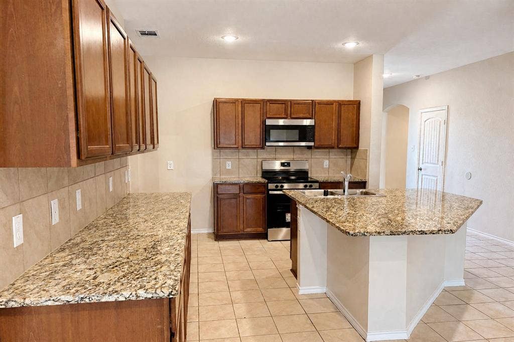 Kitchen featuring wood cabinetry, stone-finish countertops, ceramic tile backsplash, central island, and stainless steel appliances