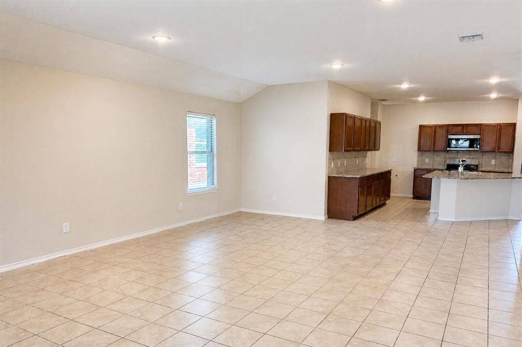 Open-concept interior featuring large-format ceramic tile flooring, recessed lighting, and a kitchen equipped with stone-surface countertops and wood cabinetry