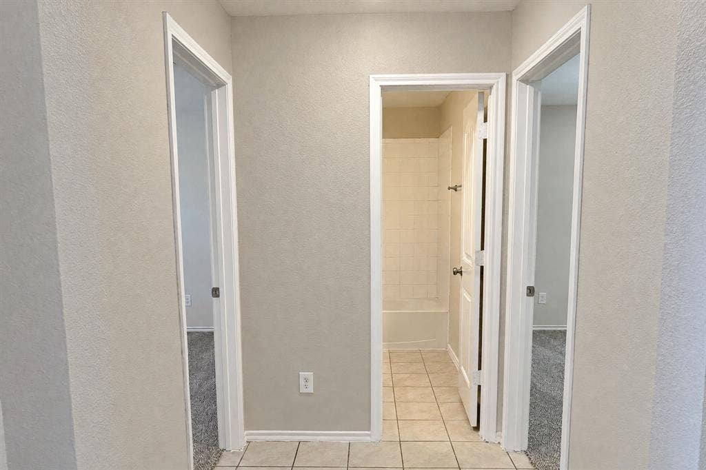 Neutral-toned interior hallway featuring tile flooring, three solid-core doors, and a tiled shower enclosure