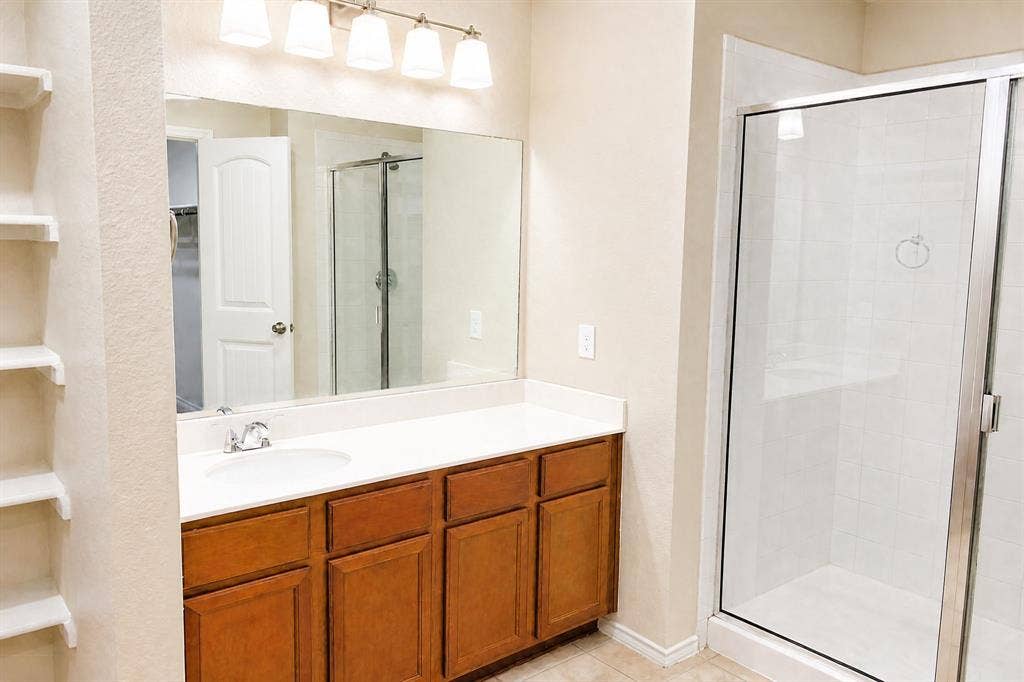 Bathroom featuring a wood-finish vanity with a stone-top counter, undermount sink, glass-enclosed shower, and built-in shelving