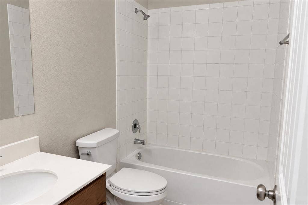 Bathroom featuring a vanity with a white countertop and integrated sink, a full-height white tile tub surround, a chrome shower fixture, and a standard bathtub