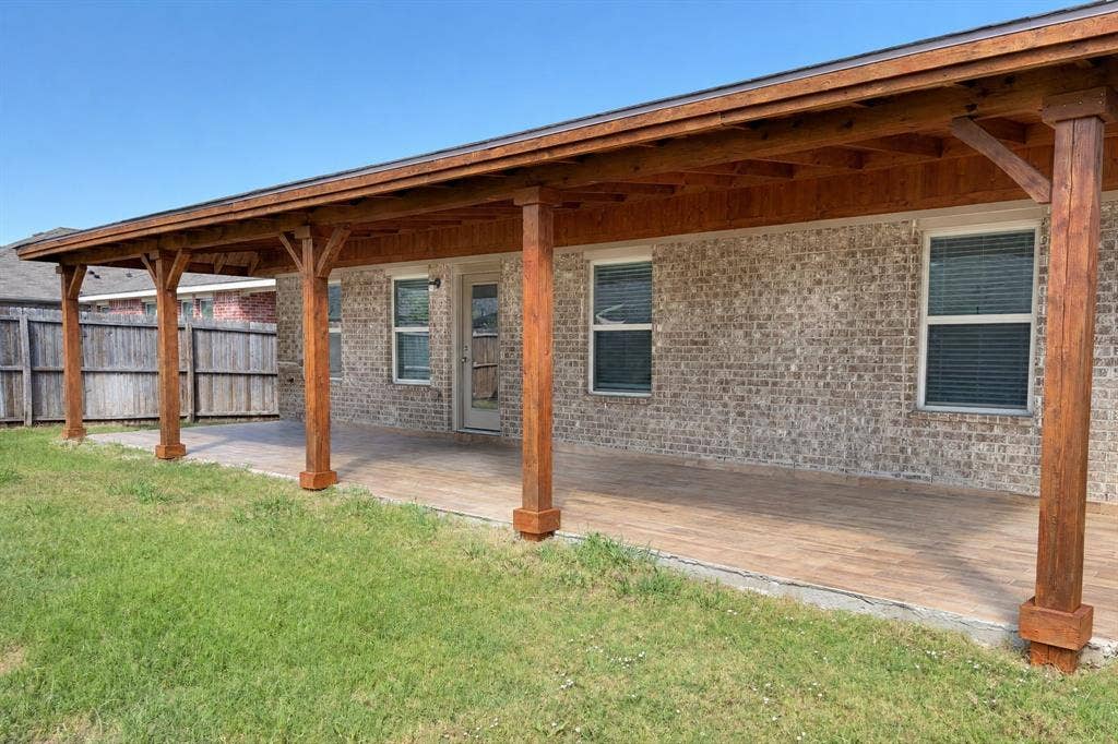 Covered patio featuring a timber-frame support structure, wood-finish flooring, brick exterior siding, and horizontal window blinds
