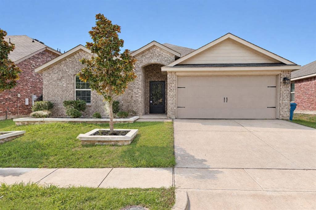 Single-story brick exterior featuring a recessed entryway, attached two-car garage, concrete driveway, and stone-bordered landscaping beds