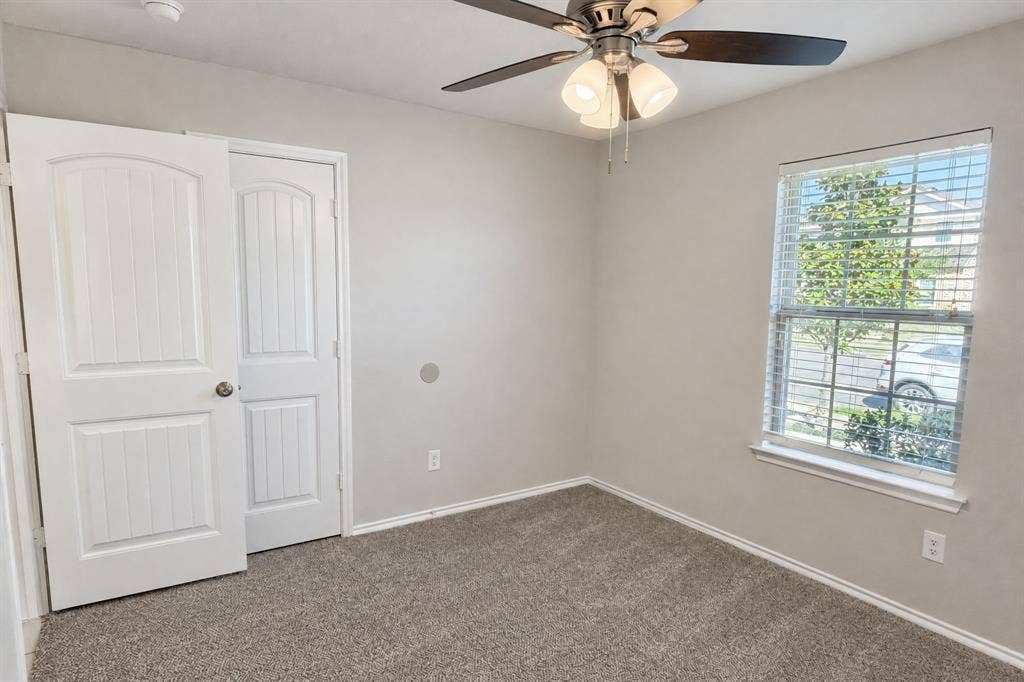 Neutral-toned room featuring neutral carpeting, a ceiling fan with integrated lighting, a single-hung window with horizontal blinds, and a paneled interior door