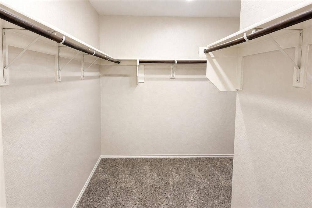 Walk-in closet featuring neutral carpeting, white wall finishes, and wrap-around built-in shelving with integrated hanging rods