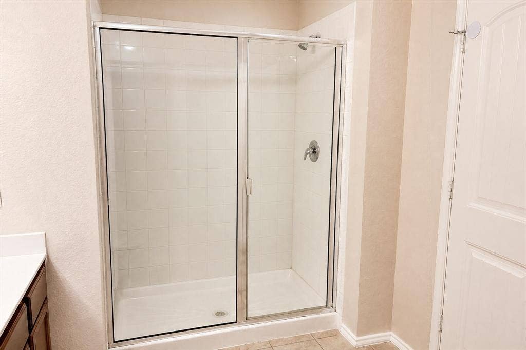 Shower enclosure with chrome-framed glass sliding doors, white tiled walls, and a single-handle faucet