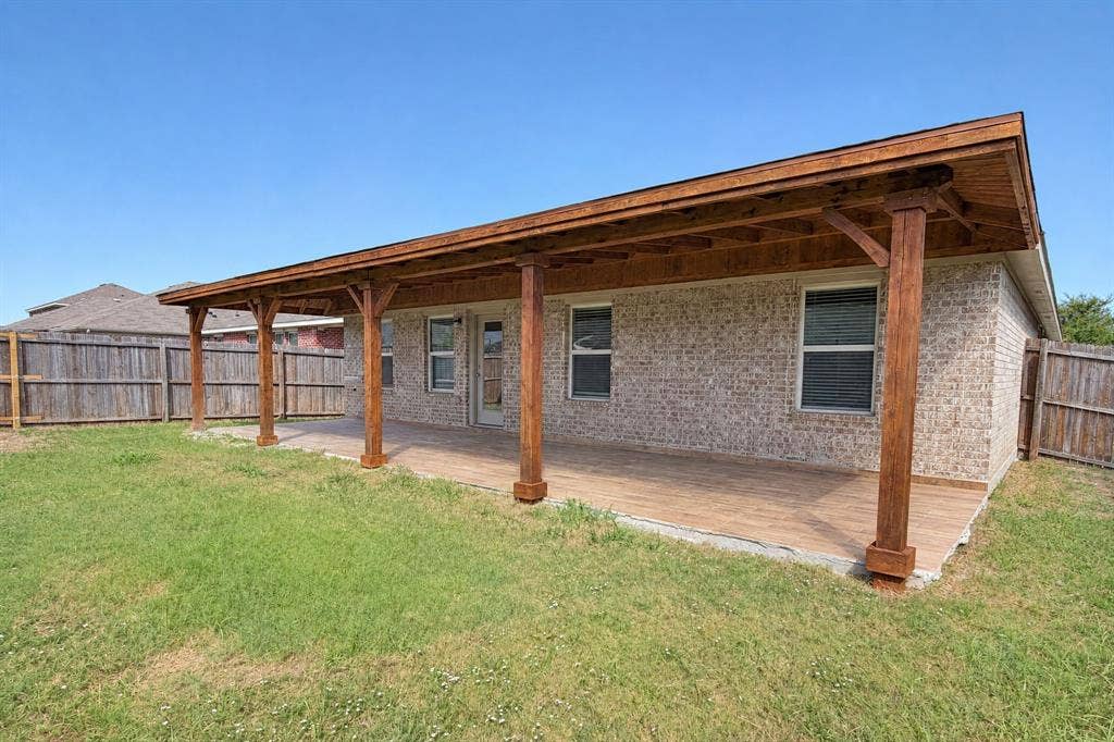 Covered patio featuring a wood-beam structure, exposed wooden ceiling, tile flooring, and brick exterior walls, enclosed by wood privacy fencing