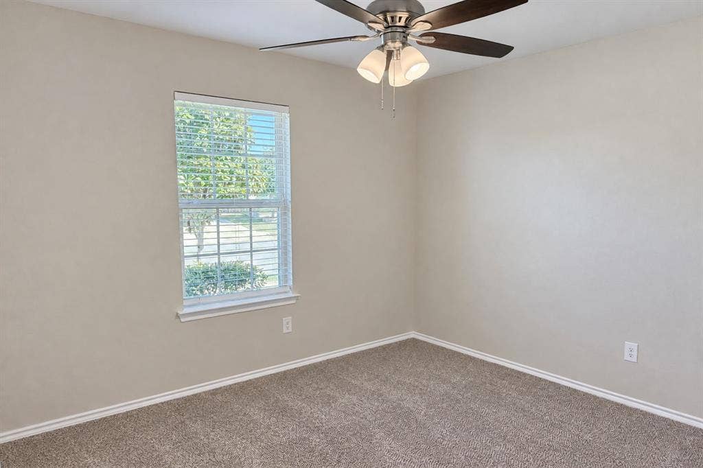 Neutral-toned interior featuring wall-to-wall carpeting, a multi-pane window with blinds, and a ceiling fan with integrated light fixture