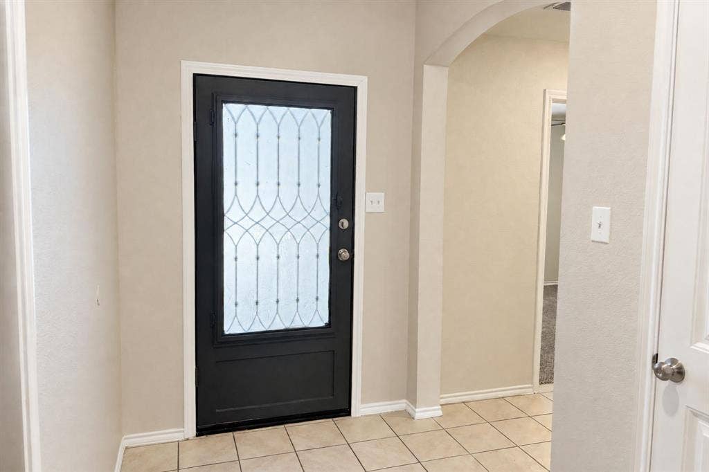 Entryway featuring a dark-toned front door with decorative glass inlay, neutral wall paint, arched architectural detail, and ceramic tile flooring