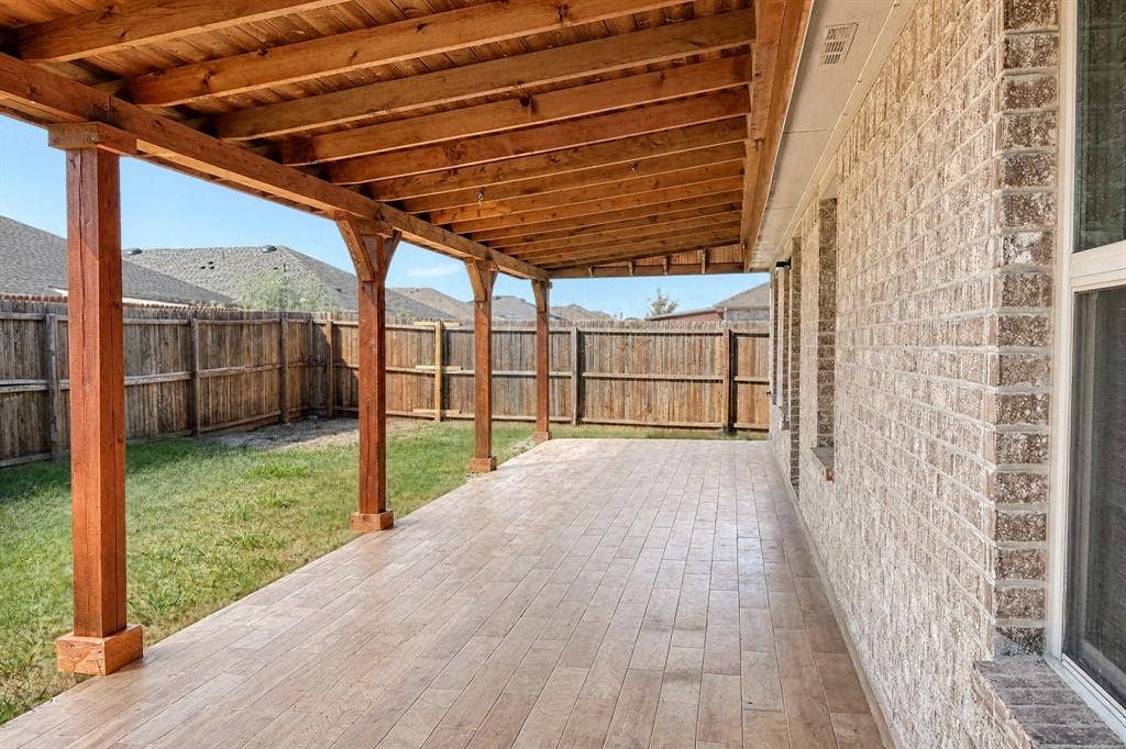 Covered patio featuring a wood-beam pergola structure, textured tile flooring, and brick exterior wall