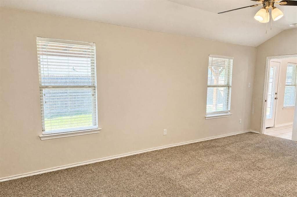 Vaulted ceiling, neutral wall tones, carpeted flooring, and multi-pane windows featuring horizontal blinds