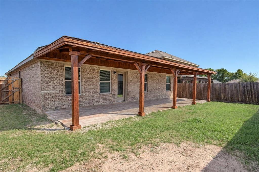 Rear exterior featuring a brick facade, expansive covered patio with wood-post supports, and wood-finish ceiling detailing