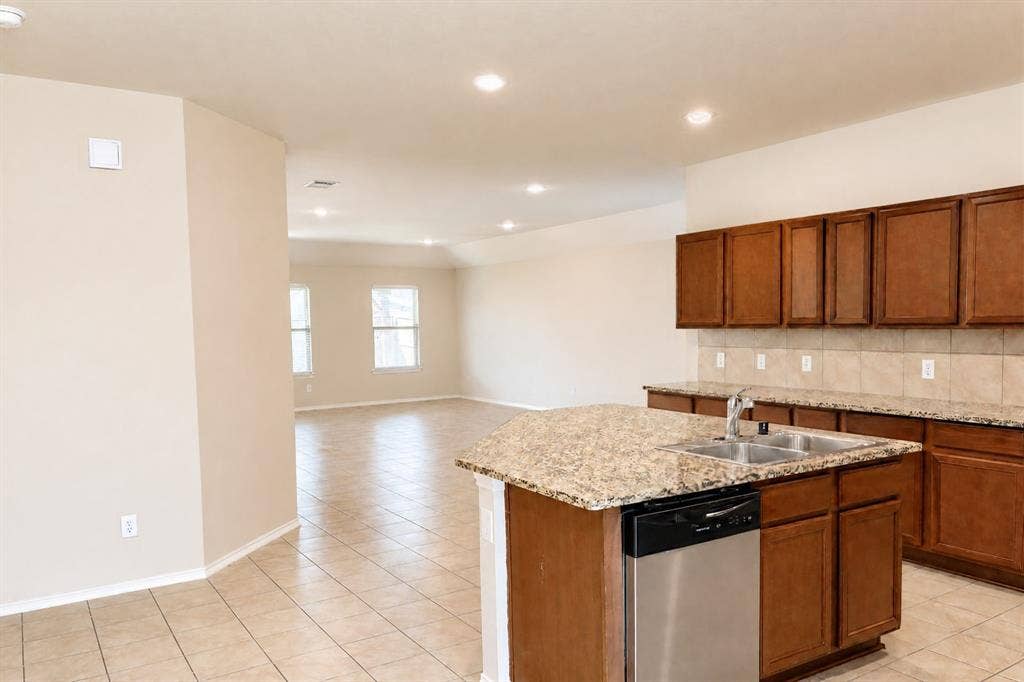 Kitchen featuring stone-finish countertops, wood cabinetry, stainless steel dishwasher, double-basin undermount sink, and tile flooring