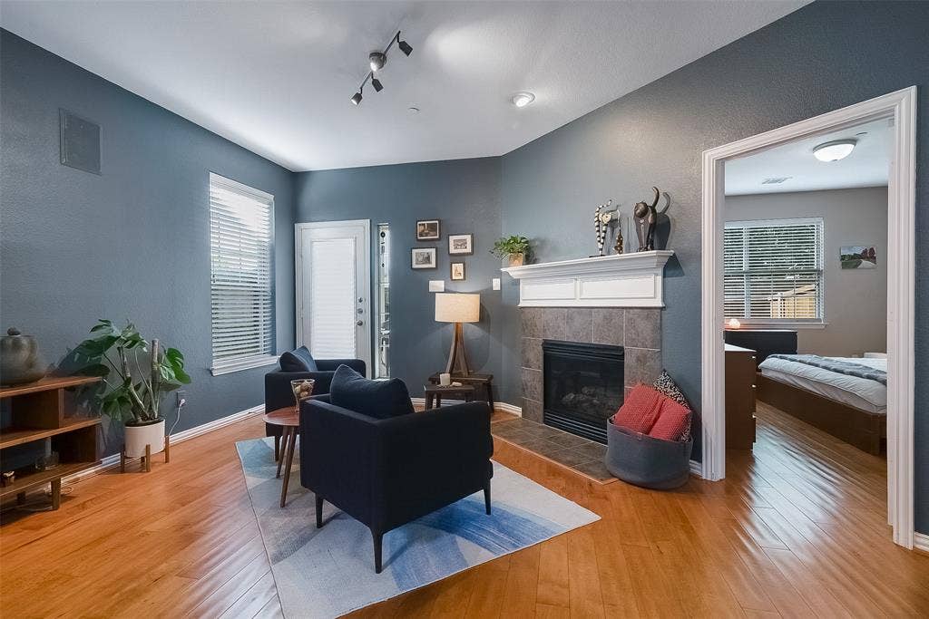 Living area featuring wood-finish flooring, a fireplace with a stone-tile surround and a prominent mantle, track lighting, and a door with a vertical glass insert