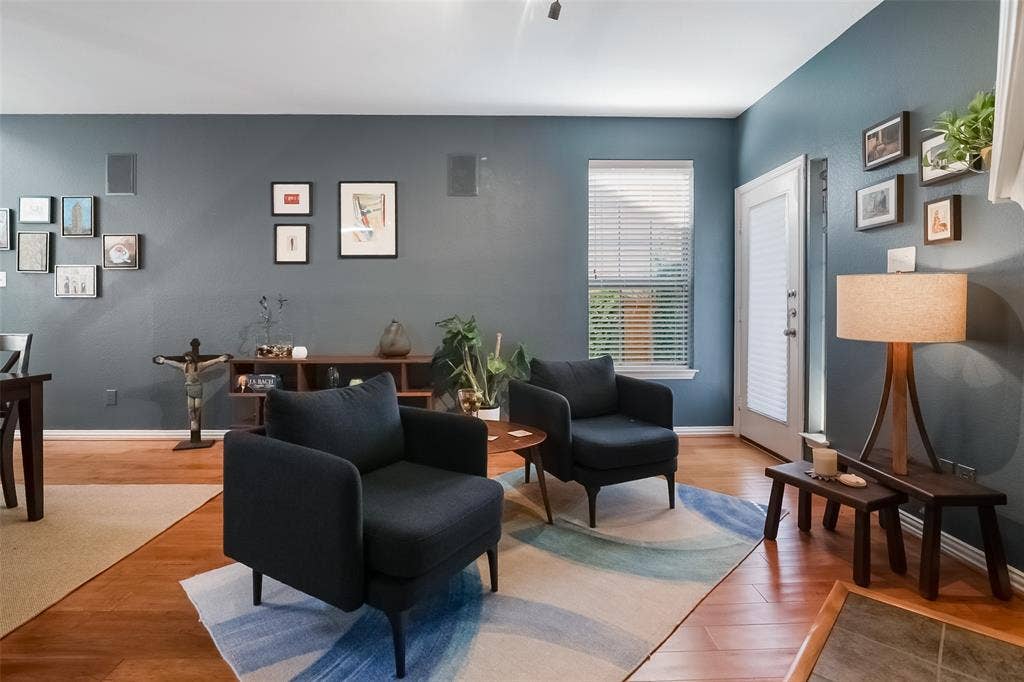 Living area featuring wood-finish flooring, a single-hung window with horizontal blinds, neutral wall paint, and integrated ceiling speakers