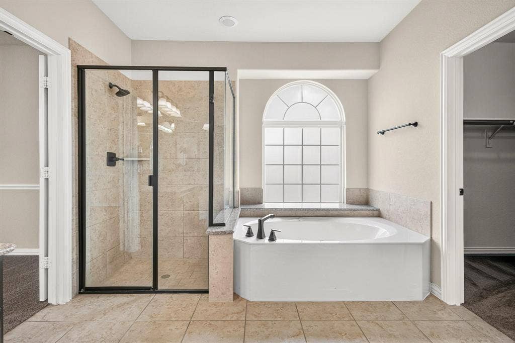 206 White Rock Court, Ovilla, TX 75154 Glass-enclosed shower with tile surround, soaking tub with arched window, and stone-finish tile flooring
