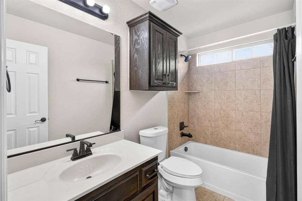 206 White Rock Court, Ovilla, TX 75154 Vanity with a solid-surface countertop and integrated oval sink, dark wood-finish cabinetry, wall-mounted storage cabinet, matte black hardware, and a tub-shower combination with tiled surround
