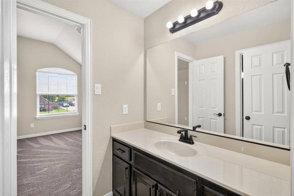 206 White Rock Court, Ovilla, TX 75154 Vanity featuring a solid-surface countertop, integrated oval sink, matte black faucet, dark wood-finish cabinetry, and a full-width mirror with a four-light fixture