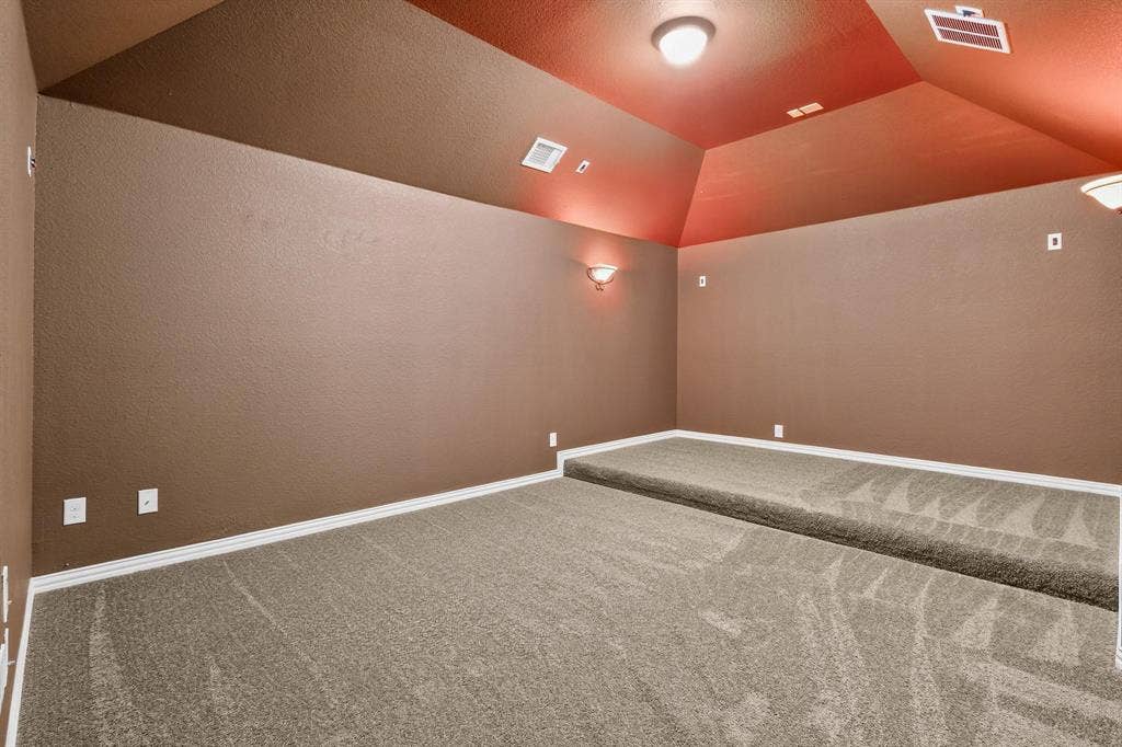 206 White Rock Court, Ovilla, TX 75154 Interior space featuring a raised tiered floor, vaulted ceiling, neutral wall-to-wall carpeting, wall-mounted sconce lighting, and flush-mount overhead lighting