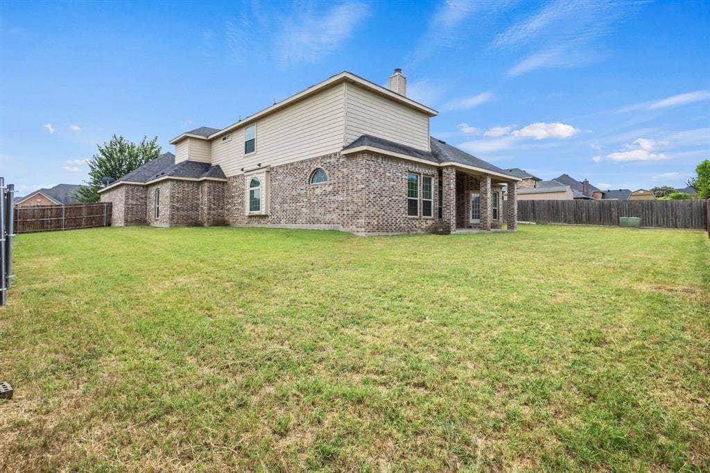 206 White Rock Court, Ovilla, TX 75154 Expansive backyard featuring a manicured lawn, brick and siding exterior, covered patio, arched windows, and wood fencing