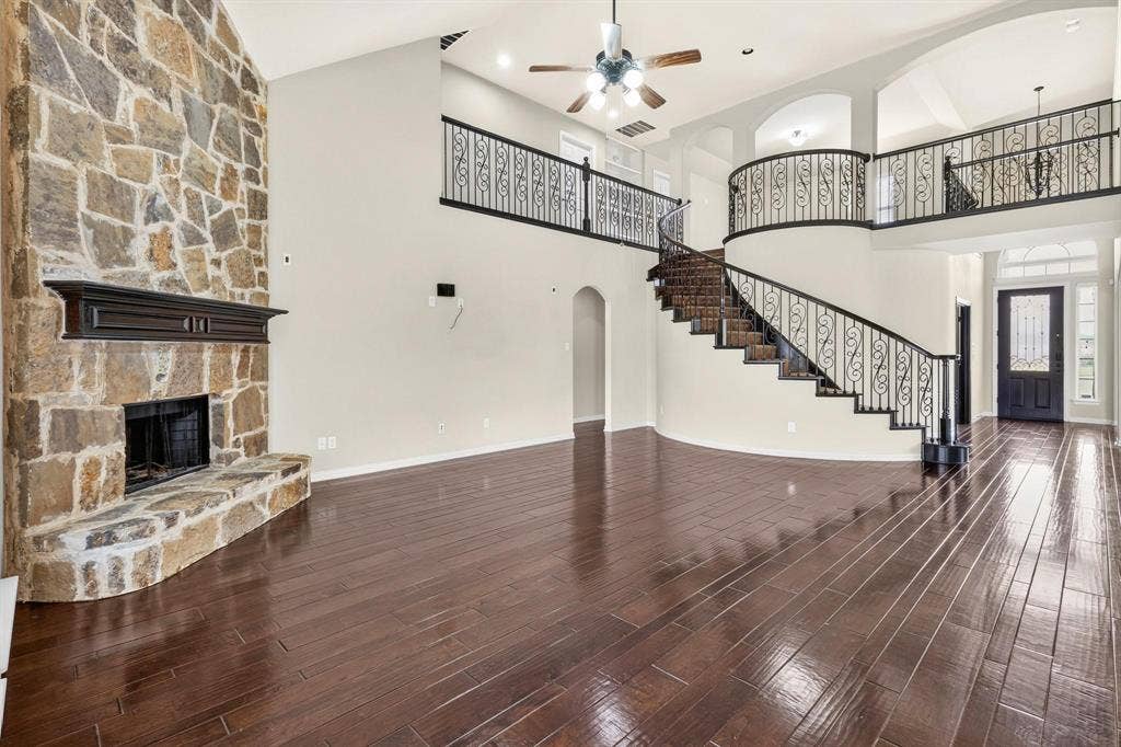 206 White Rock Court, Ovilla, TX 75154 Double-height living area featuring a full-height stone masonry fireplace, wood-finish flooring, a curved staircase with ornate iron railing, and a landing overlook
