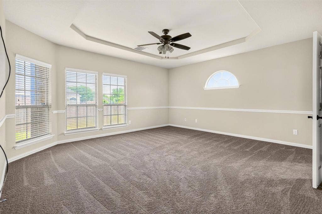 206 White Rock Court, Ovilla, TX 75154 Interior room featuring a tray ceiling, ceiling fan, carpeting, windows with horizontal blinds, and a semi-circular accent window with chair rail molding