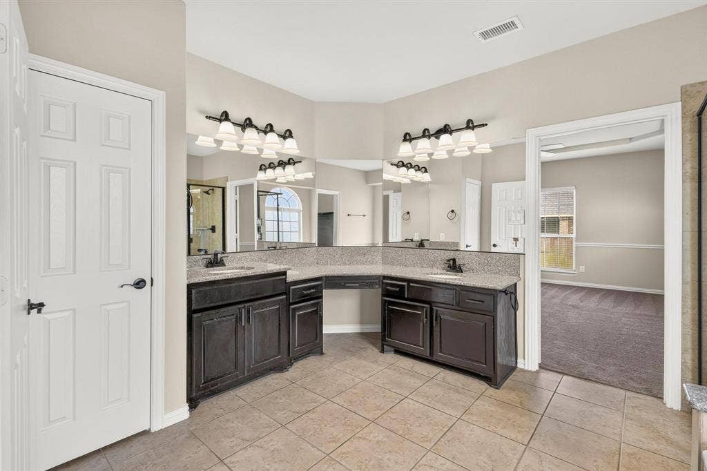 206 White Rock Court, Ovilla, TX 75154 Double vanity with a central seated makeup station, stone-surfaced countertop, dual under-mount sinks, dark-finish cabinetry, and multi-bulb vanity lighting