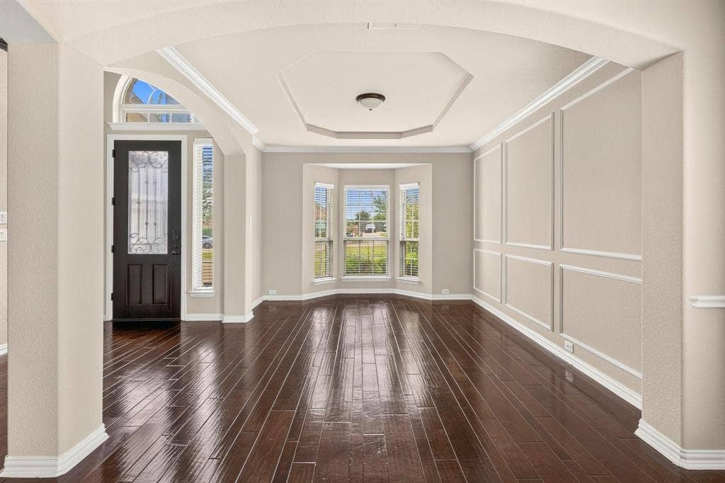 206 White Rock Court, Ovilla, TX 75154 Formal dining area featuring wood-finish flooring, a tray ceiling, wainscoting, an arched entryway, and a bay window