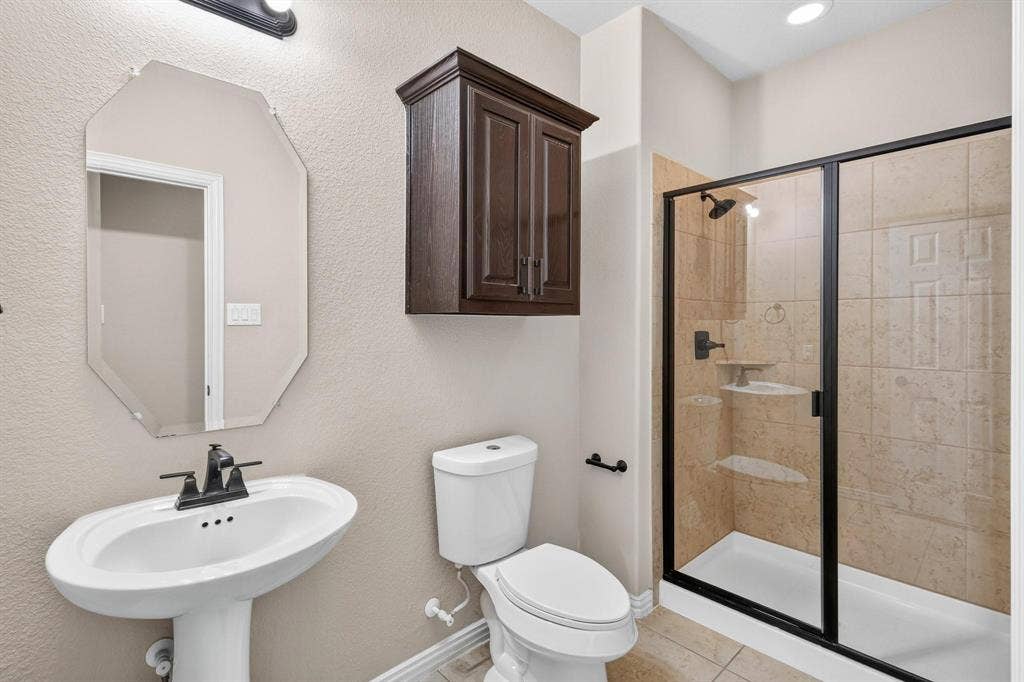 206 White Rock Court, Ovilla, TX 75154 Bathroom featuring a pedestal sink with a matte black faucet, wall-mounted dark wood cabinetry, an octagonal mirror, and a walk-in shower with tiled surround and black-framed glass enclosure