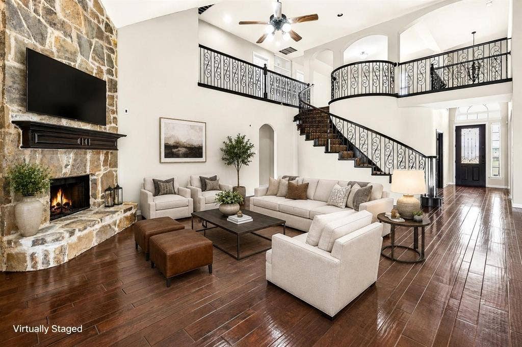 206 White Rock Court, Ovilla, TX 75154 High-ceilinged living area featuring a floor-to-ceiling stone fireplace, wood-finish flooring, curved staircase with ornamental metal railing, and arched architectural detailing