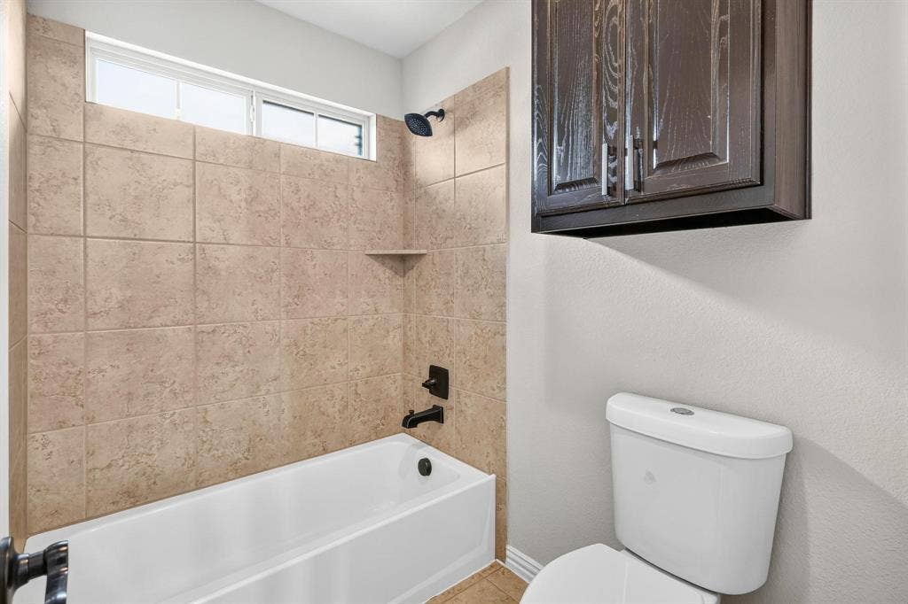 206 White Rock Court, Ovilla, TX 75154 Bathroom featuring a shower-tub combination with tan ceramic wall tile, dark-finish hardware, built-in cabinetry, and a transom window