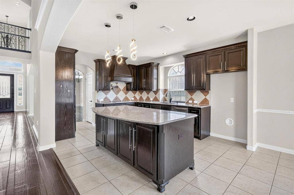 206 White Rock Court, Ovilla, TX 75154 Kitchen featuring dark-finish cabinetry, central island with stone-surface countertop, decorative tile backsplash, pendant lighting, and arched window