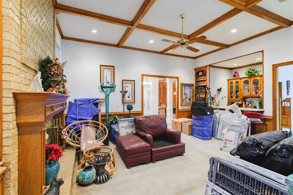 Living area featuring a coffered wood ceiling, brick fireplace with a wood mantel, built-in wooden shelving, and recessed lighting