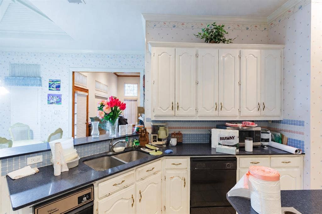 Kitchen featuring white cabinetry, dark countertops, a double-basin stainless steel sink with a pull-down faucet, and a black built-in dishwasher