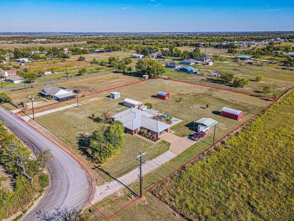 1158 County Road 141, Kaufman, TX 75142 Expansive rural acreage featuring a single-story residence, multiple detached storage structures, an open-sided carport, and a paved driveway