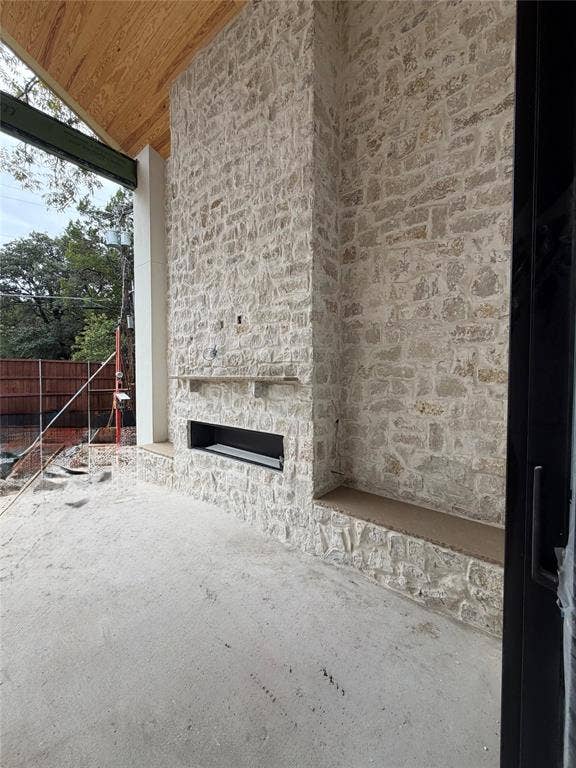 Covered outdoor patio featuring a floor-to-ceiling stone masonry fireplace, integrated stone hearth seating, a linear firebox, and a wood-plank ceiling