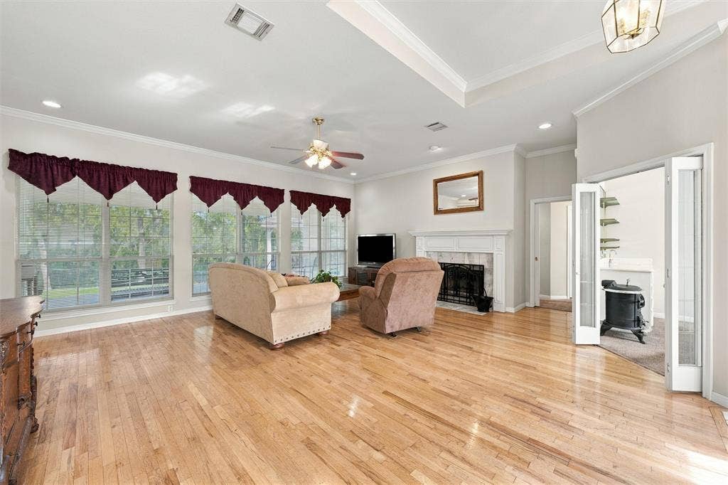 5030 Bosque Ridge Road, Crawford, TX 76638 Living area featuring wood-finish flooring, tray ceiling, fireplace with detailed mantel, recessed lighting, and large windows with natural illumination