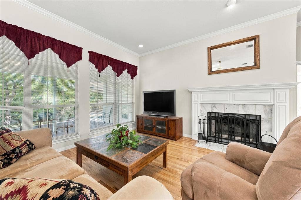 5030 Bosque Ridge Road, Crawford, TX 76638 Living area featuring wood-finish flooring, floor-to-ceiling windows, and a fireplace with a white mantel and stone surround