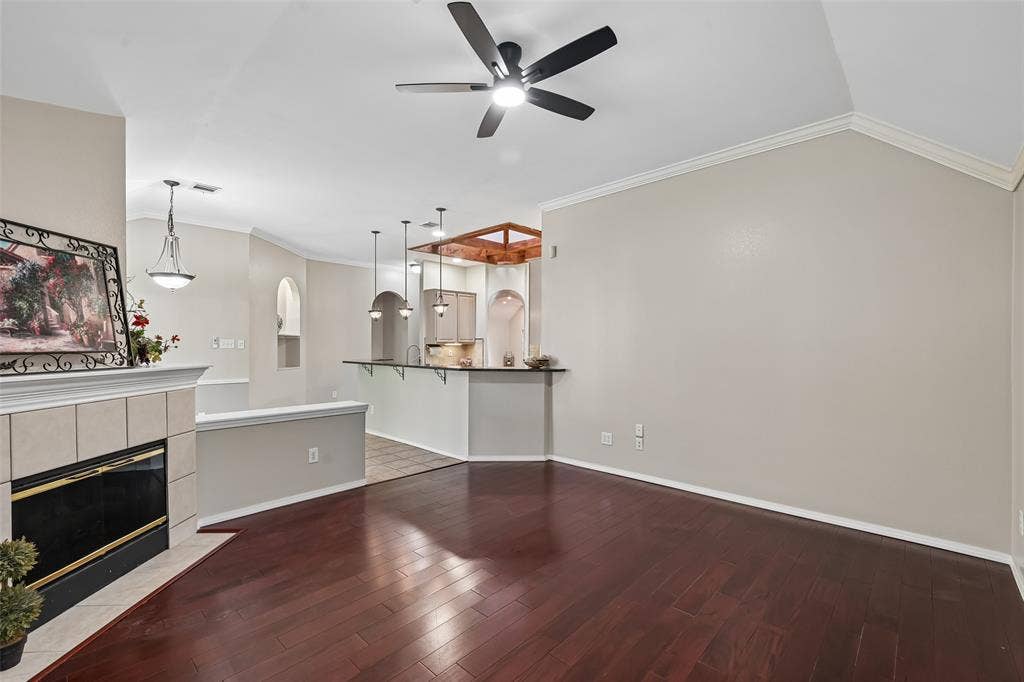 3837 Pine Valley Drive, Plano, TX 75025 Vaulted ceilings, wood-finish flooring, tiled fireplace surround, integrated kitchen breakfast bar, and pendant lighting