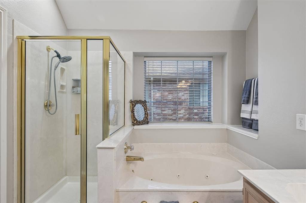 3837 Pine Valley Drive, Plano, TX 75025 Jetted soaking tub with stone-finish surround, glass-enclosed shower with gold-tone frame, handheld shower fixture, and recessed window sill