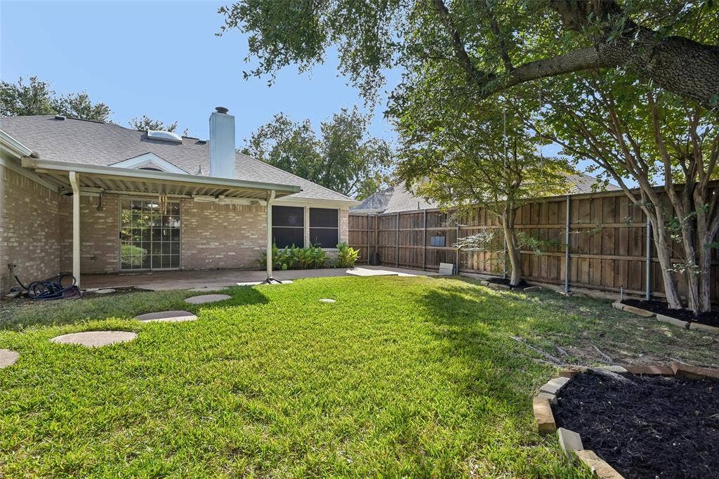 3837 Pine Valley Drive, Plano, TX 75025 Brick exterior with a covered patio, stone garden edging, wood privacy fencing, and mature trees
