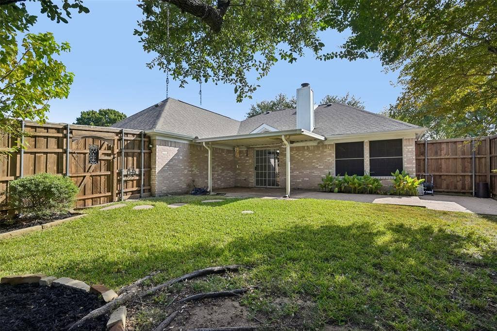 3837 Pine Valley Drive, Plano, TX 75025 Brick exterior featuring a covered patio, fenced yard, and stone-bordered landscaping
