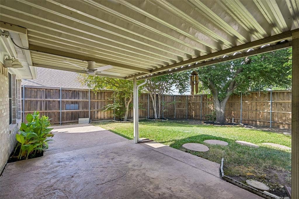 3837 Pine Valley Drive, Plano, TX 75025 Covered patio featuring a corrugated metal roof and ceiling fan, stamped concrete flooring, fenced backyard, and mature trees
