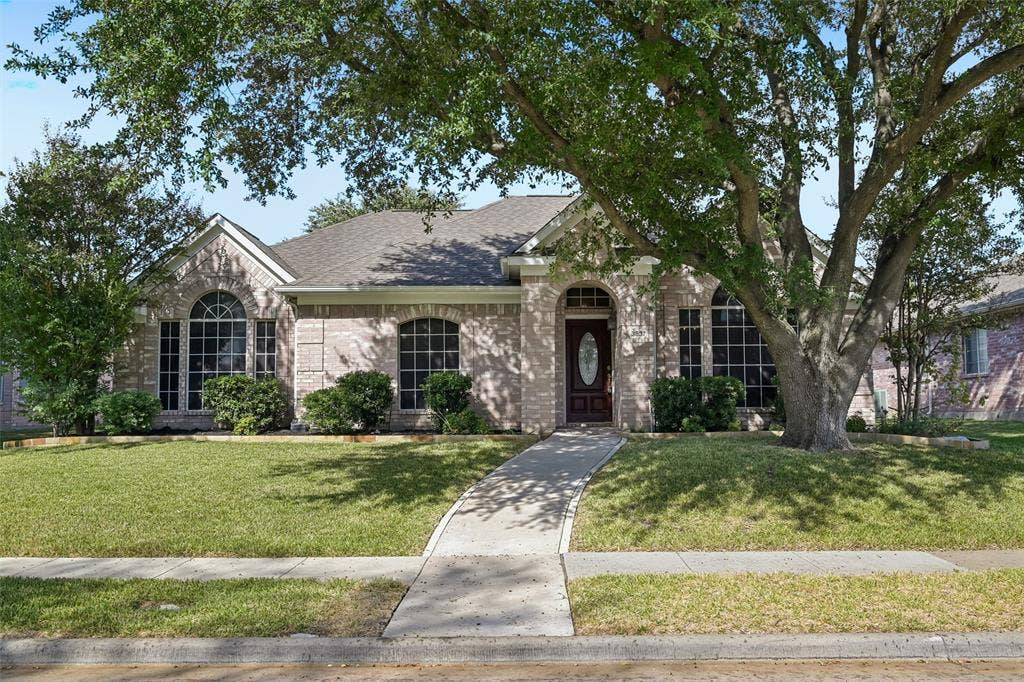 3837 Pine Valley Drive, Plano, TX 75025 Single-story brick exterior featuring an arched entryway, decorative oval-glass front door, grid-pattern windows, and mature trees
