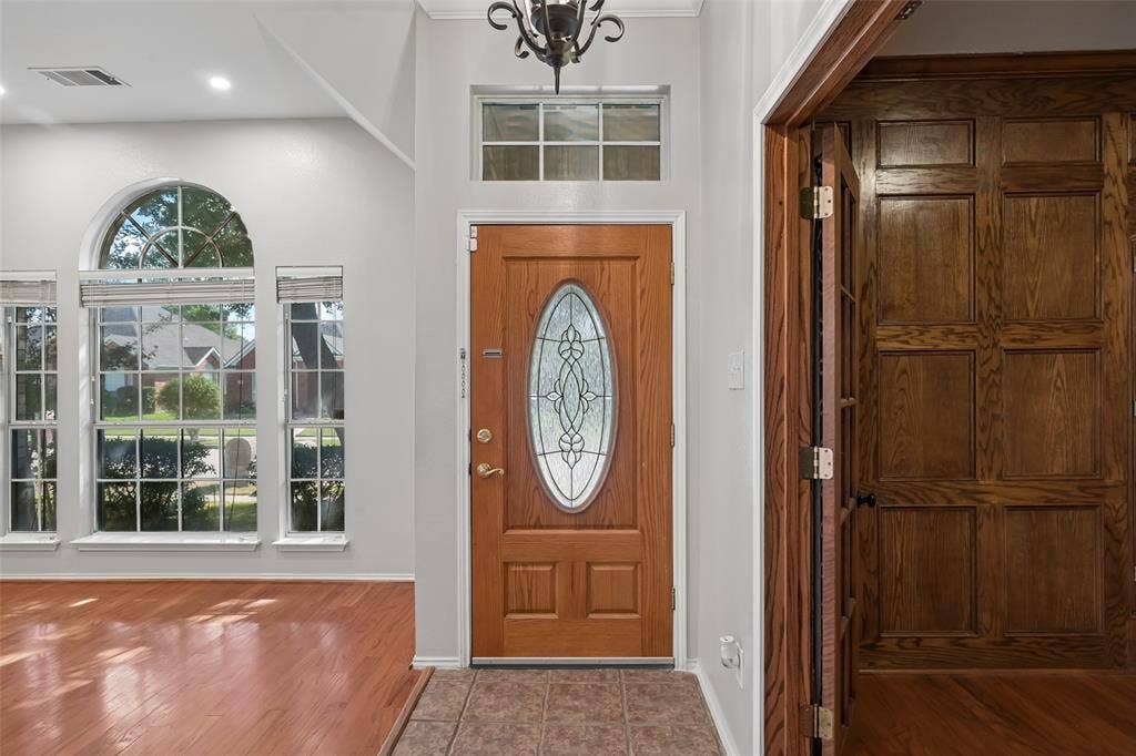 3837 Pine Valley Drive, Plano, TX 75025 Entryway featuring a wood door with an oval decorative glass insert, wood-finish flooring, tile flooring, wall-mounted wood paneling, and large multi-pane windows with arched detailing