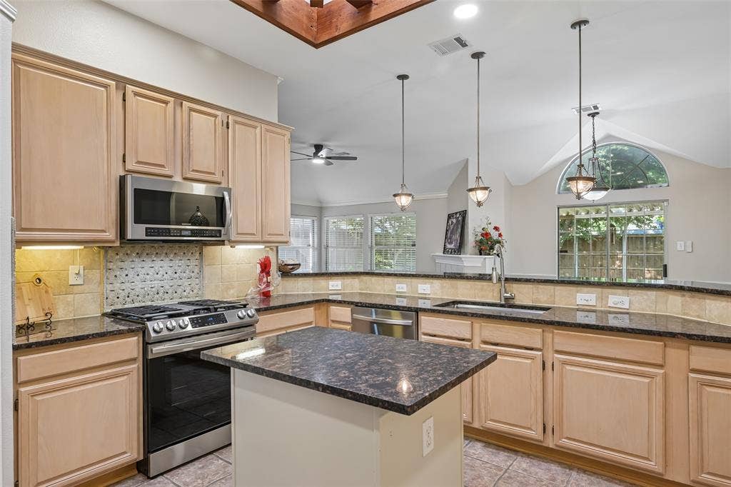 3837 Pine Valley Drive, Plano, TX 75025 Kitchen featuring natural wood cabinetry, dark stone countertops, stainless steel appliances, a central island, and a decorative tile backsplash