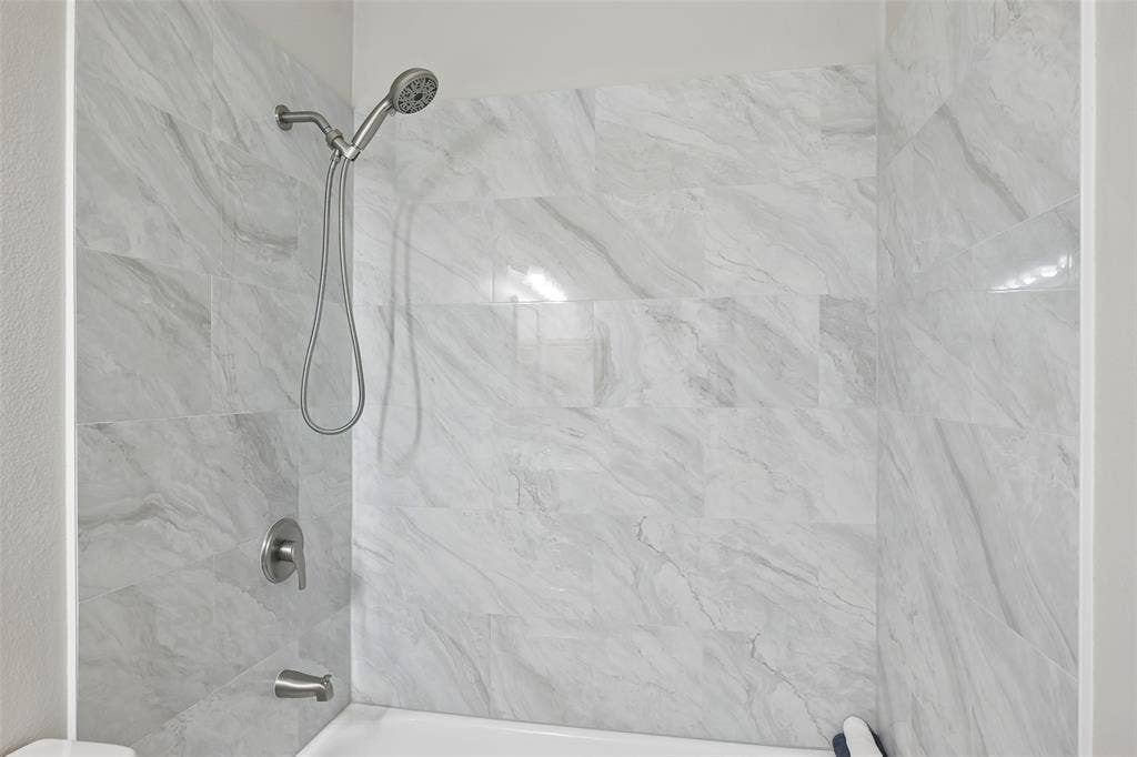 3837 Pine Valley Drive, Plano, TX 75025 Shower enclosure featuring large-format stone-finish tile surround, brushed nickel finish handheld showerhead, matching single-handle pressure balance valve, and tub spout