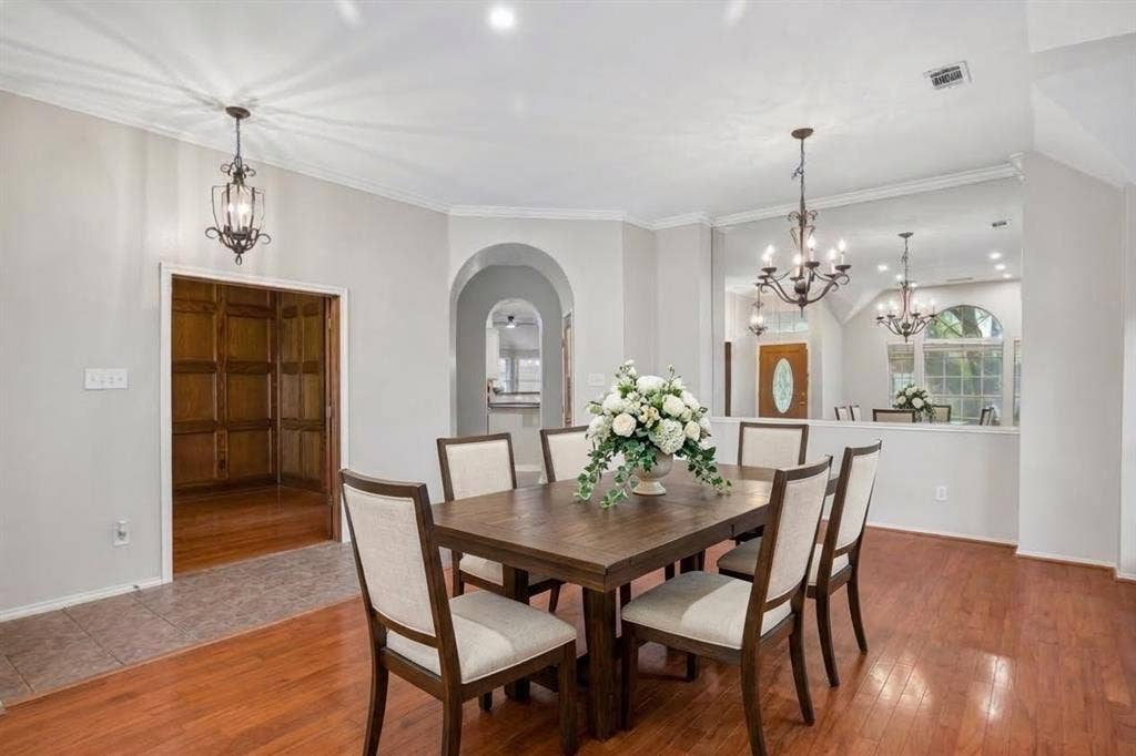 3837 Pine Valley Drive, Plano, TX 75025 Interior space featuring wood-finish flooring, two decorative iron chandeliers, a large built-in mirror, an arched entryway, and wood-paneled walls